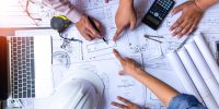 engineers pointing to building on blueprint and using laptop to drawing design building Project in office, construction concept. Engineer concept